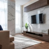 Modern TV set hanging on wall between wooden cabinets in front of comfortable sofa in light living room